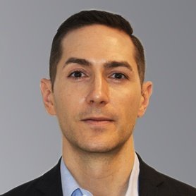 Bio photo of Colin Cuniff wearing a blue button-up shirt and a black blazer